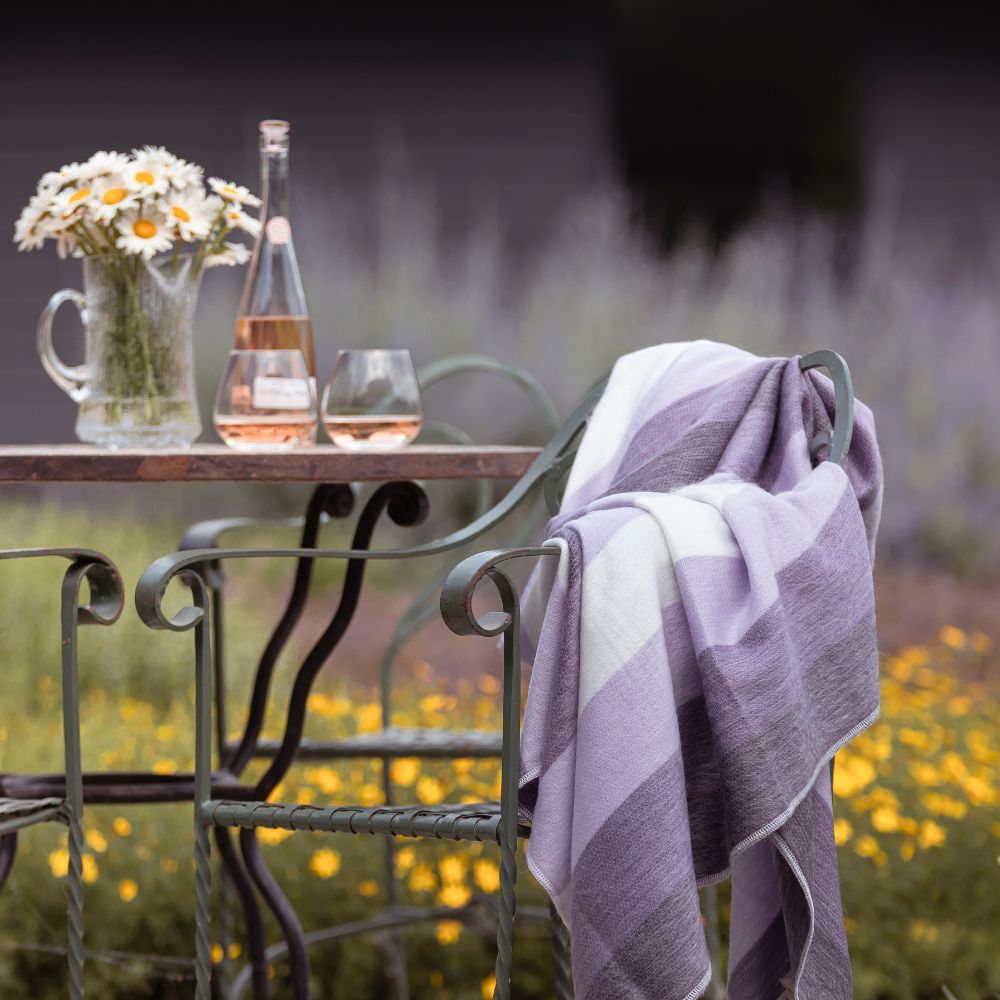 Outdoor table with rosé wine, daisies, and striped blanket nearby