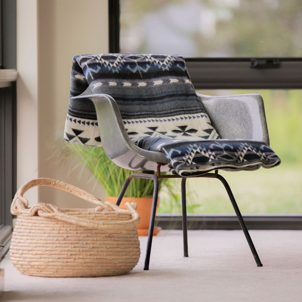 A cozy chair with a soft blanket draped over it, accompanied by a woven basket on the floor beside it.