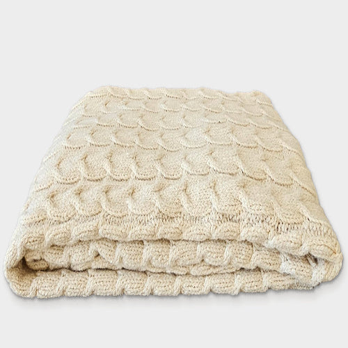 A beige cable knit throw made of organic pima cotton and undyed baby alpaca wool.