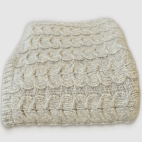 A beige cable knit throw made of organic pima cotton and undyed baby alpaca wool.