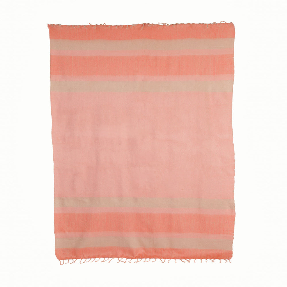A striped throw blanket in shades of pink and camel with white fringed edges.
