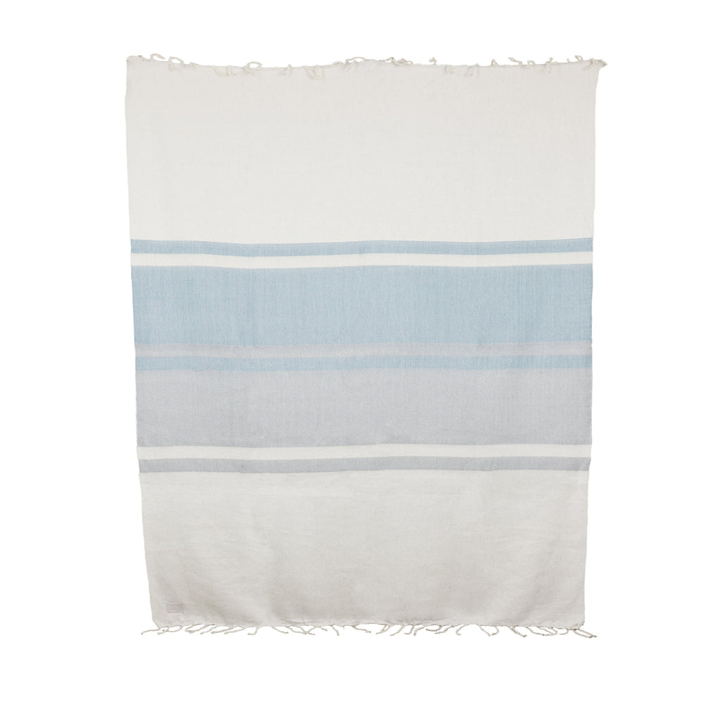 A striped throw blanket with white, bluish gray, and gray horizontal stripes, featuring hand-tied natural fringe on the long ends.
