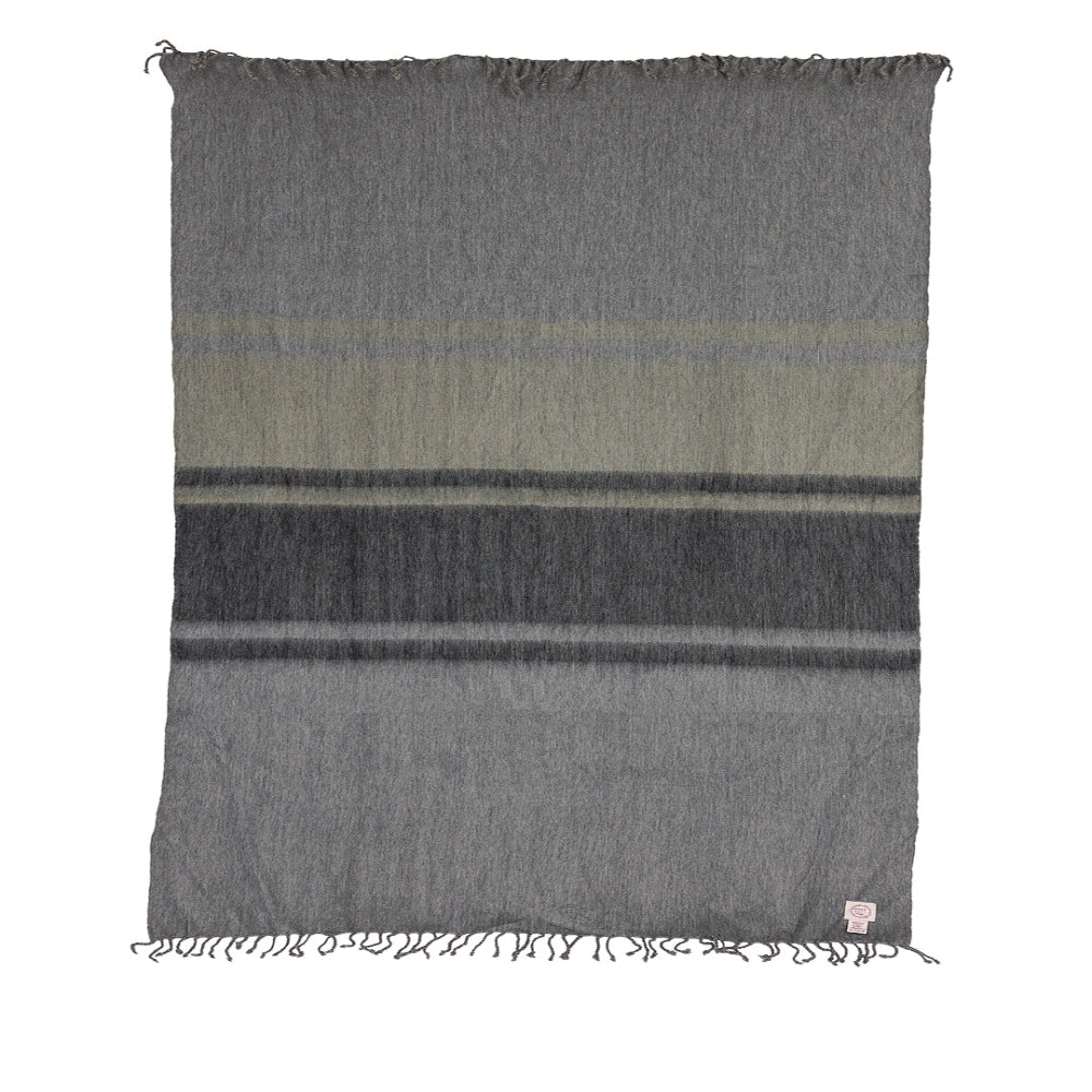 A medium-sized throw blanket with a geometric pattern in medium and dark grays and green, with hand-tied fringe on the long ends.