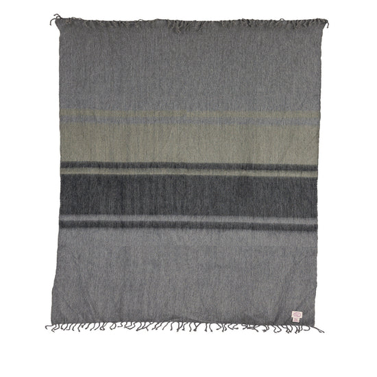 A medium-sized throw blanket with a geometric pattern in medium and dark grays and green, with hand-tied fringe on the long ends.