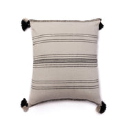 A handloomed alpaca wool pillow with ink and ivory pinstripe pattern and black pom poms on the corners.