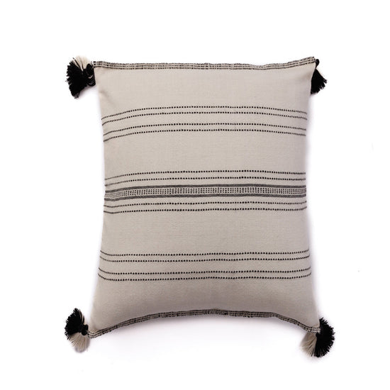 A handloomed alpaca wool pillow with ink and ivory pinstripe pattern and black pom poms on the corners.