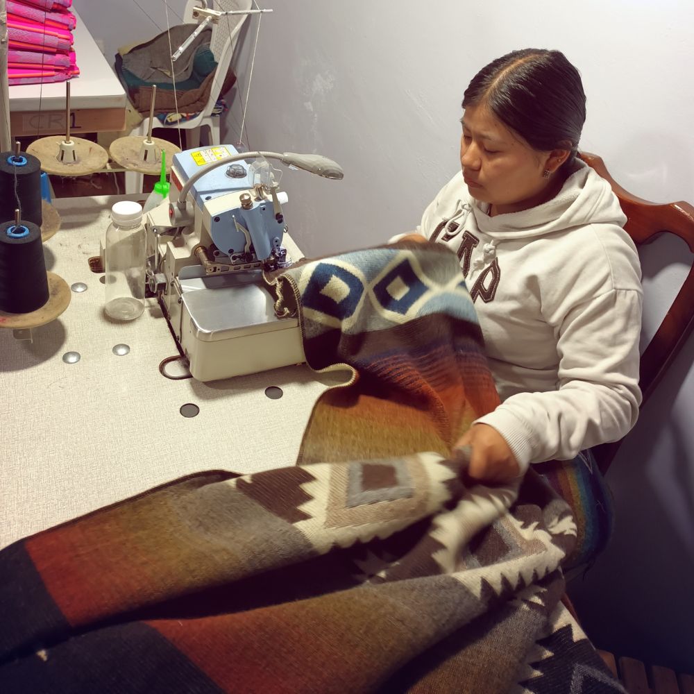 Person sewing colorful geometric fabric at table with threads and tools