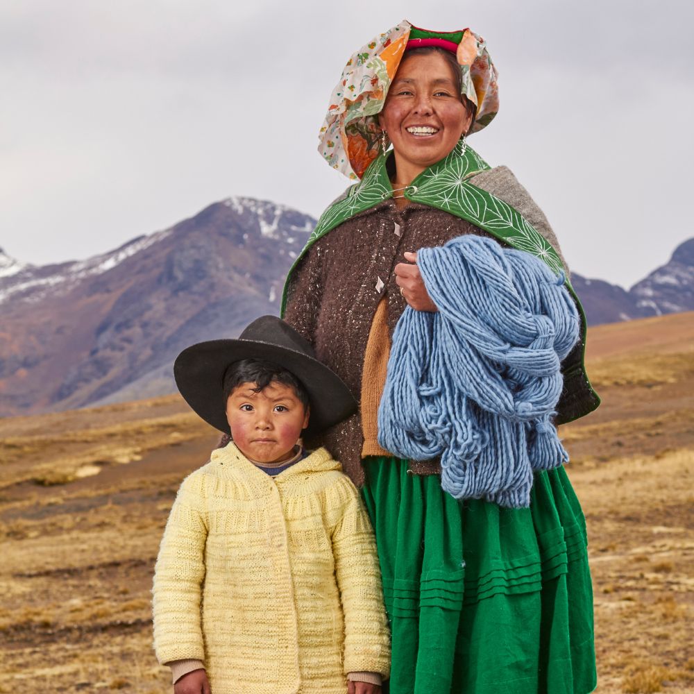 Two people in traditional clothing holding yarn in snowy mountain landscape