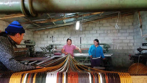 Three people weaving colorful threads on a traditional loom in rustic workshop