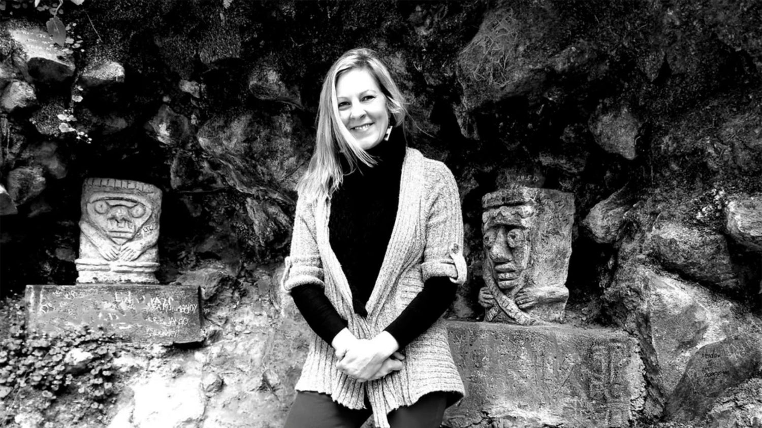 Person at archaeological site flanked by ancient stone carvings with headdresses