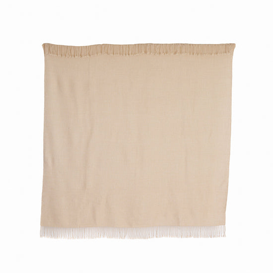 A beige, undyed ivory mist baby alpaca throw with fringes displayed against a white background.
